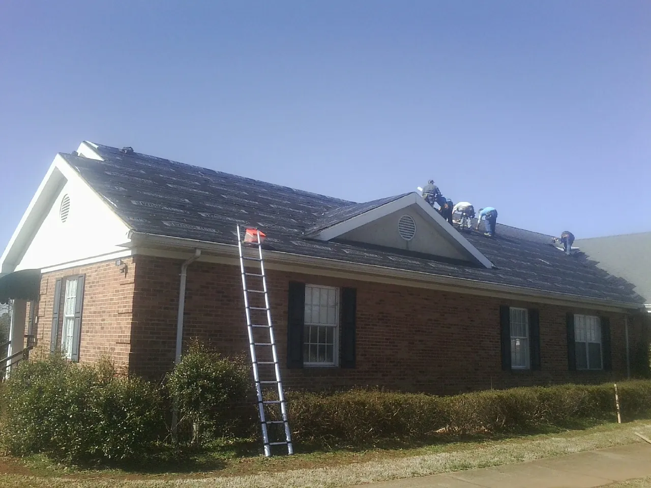 Crew tearing shingles off a brick ranch roof with a ladder set — Metal Roof Repair work by our crew in West Linn