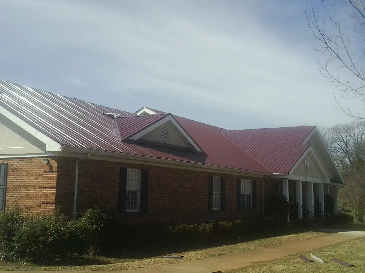 Red metal roof with gabled entries on a long brick building, from a Hail Damage Roof Repair job in West Linn