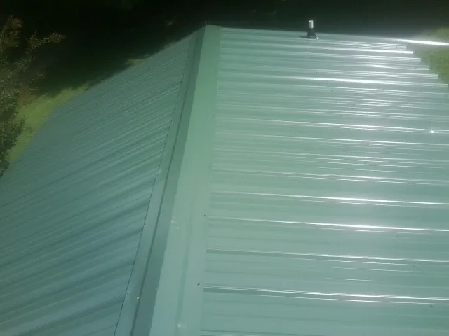 New green metal panels meeting at the ridge of a roof — Flat Roof Repair work by our crew in West Linn