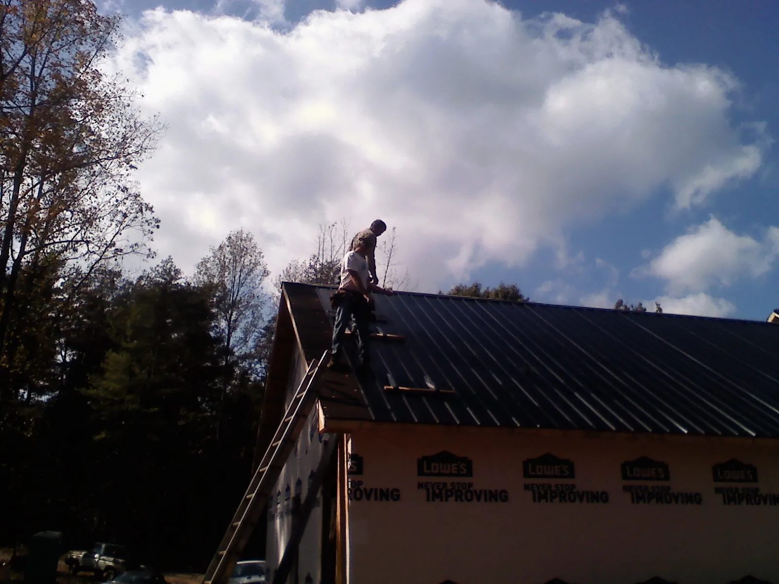 Roofer fastening dark metal panels high against a cloudy sky, from a Roof Inspection job in West Linn