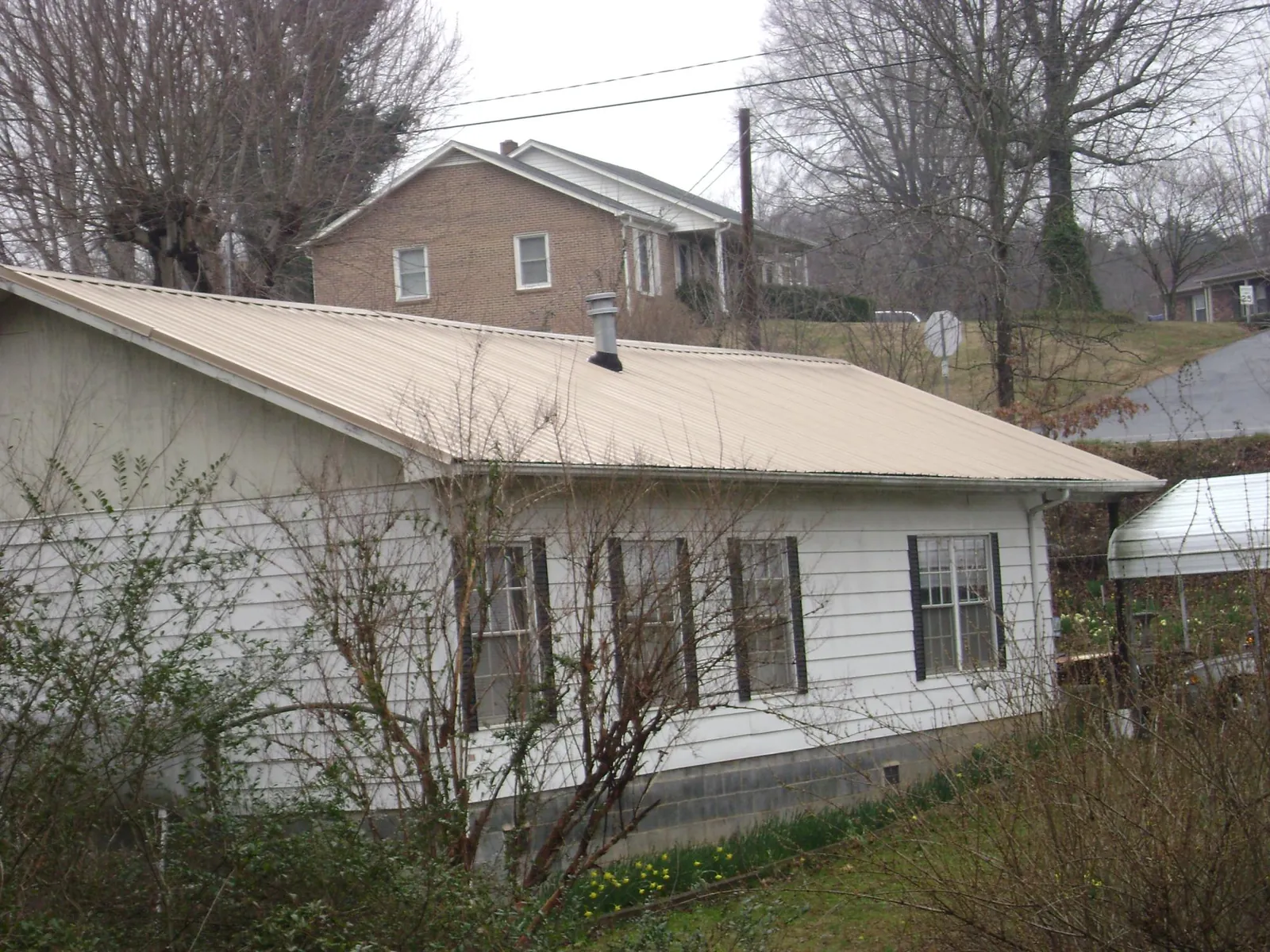 Tan metal roof on a white sided house set into a hillside — Commercial Roofing by Roofing Brothers in West Linn